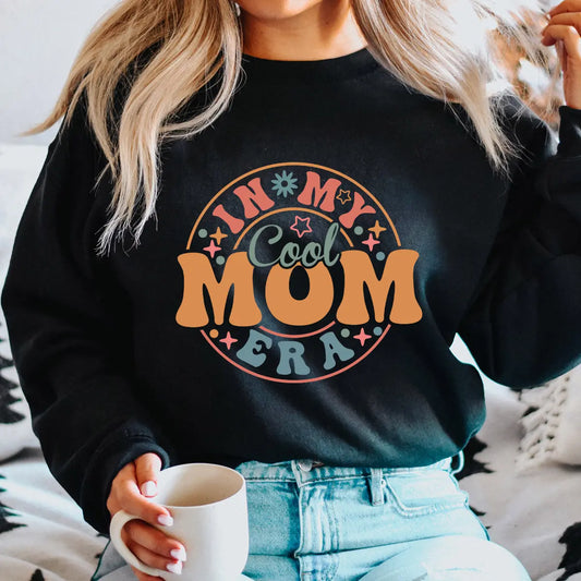 Woman wearing black sweatshirt with retro orange and teal In My Cool Mom Era print—perfect example of DTF Transfers ready to press for Mother’s Day.
