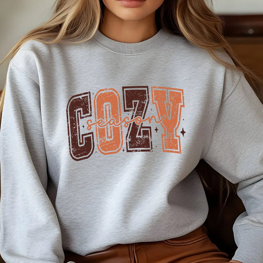 Light grey sweatshirt with "Cozy Season" DTF transfer design in warm autumn colors, perfect for creating fall-inspired boutique apparel.