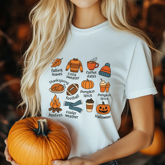 White t-shirt with colorful fall-themed doodles and words like pumpkins, bonfires, coffee, and cozy sweater, perfect for autumn-inspired custom shirts.