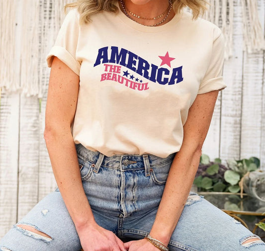 America The Beautiful - 4th of July Ready-to-Press DTF Transfer on a cream-colored t-shirt featuring navy and red typography with a star accent.