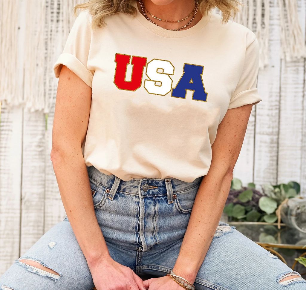 USA Bold Vintage Stitch - 4th of July Ready-to-Press DTF Transfer featuring red, white, and blue block letters with a stitched effect on a cream-colored t-shirt.