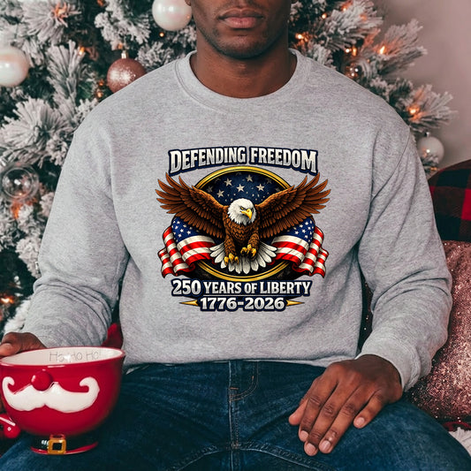Person wearing a gray sweatshirt with an eagle and American flag design, sitting in front of a decorated Christmas tree. USA 250th Anniversary 1776-2026 DTF transfer ready-to-press for custom apparel and uv dtf stickers for tumblr and bottles.