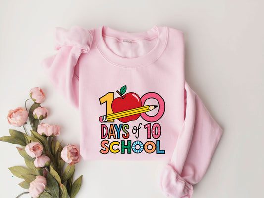 "100 Days of School" DTF transfer design on a pink sweatshirt featuring colorful letters, a red apple, and a yellow pencil, perfect for 100th-day-of-school celebrations.