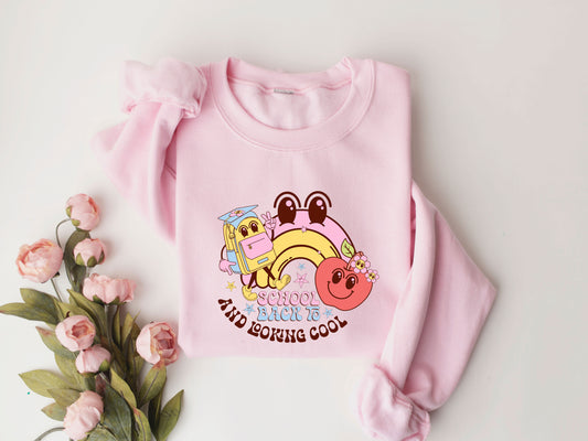 "Back to School and Looking Cool" DTF transfer design on a pink sweatshirt featuring a colorful rainbow, smiling apple with flowers, and an animated backpack, perfect for cheerful back-to-school apparel.