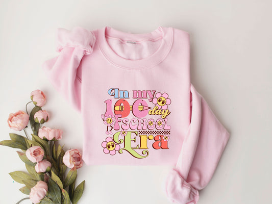 "In My 100 Day of School Era" DTF transfer design on a pink sweatshirt featuring colorful retro fonts, floral accents, and playful school-themed graphics, perfect for 100th-day-of-school celebrations.