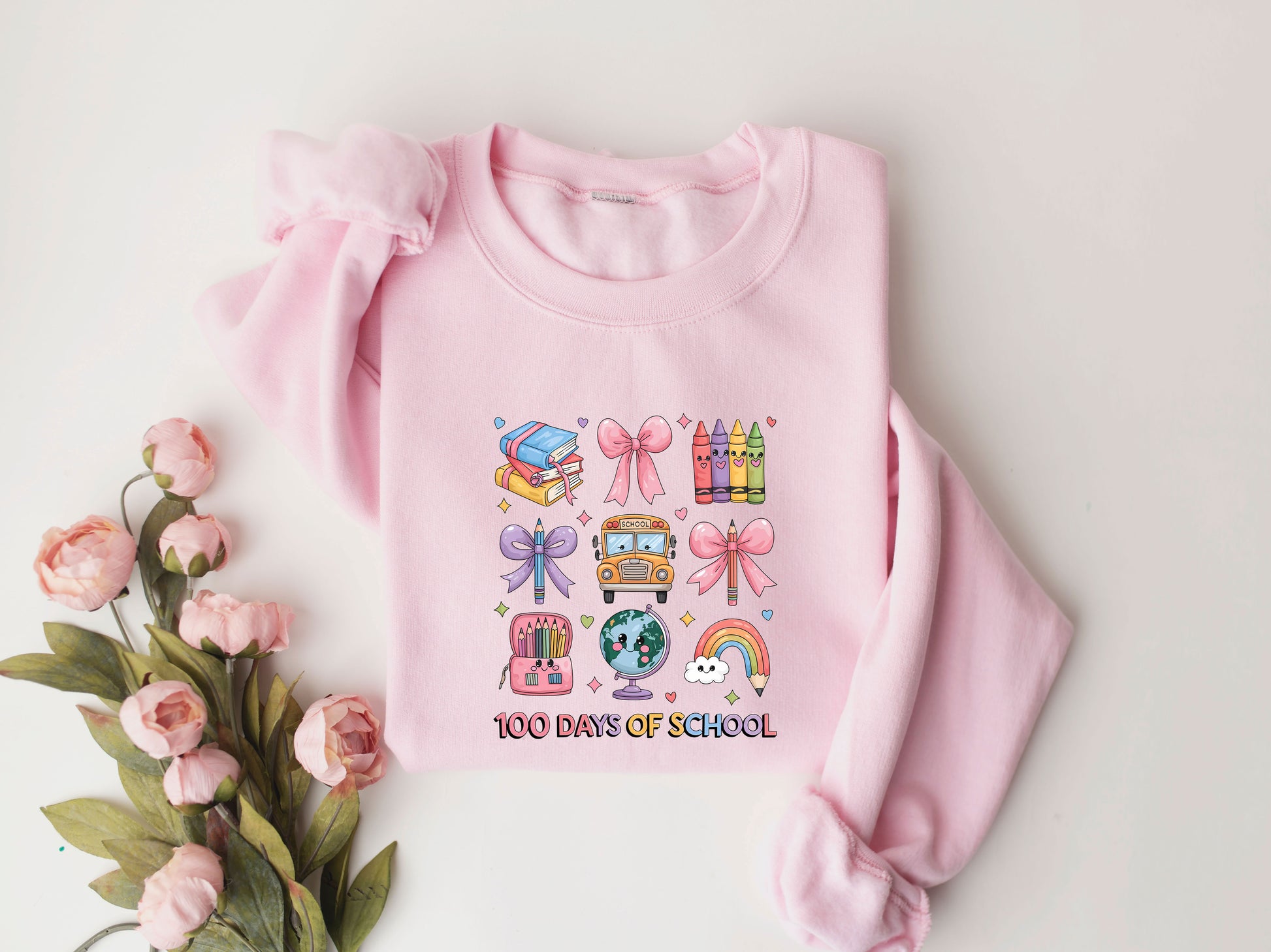 "100 Days of School" DTF transfer design on a pink sweatshirt featuring colorful icons like books, crayons, bows, a school bus, a backpack, a globe, and a rainbow, perfect for 100th-day-of-school celebrations.