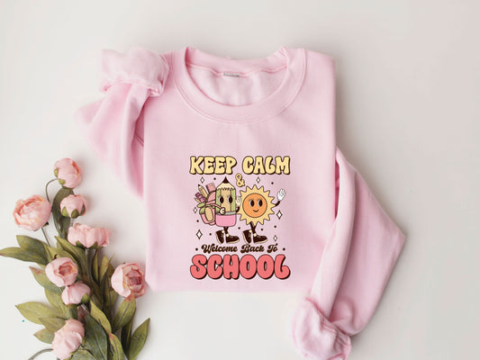 "Keep Calm & Welcome Back to School" DTF transfer design on a pink sweatshirt featuring a smiling sun, animated pencil with school supplies, and fun text, perfect for cheerful back-to-school apparel.