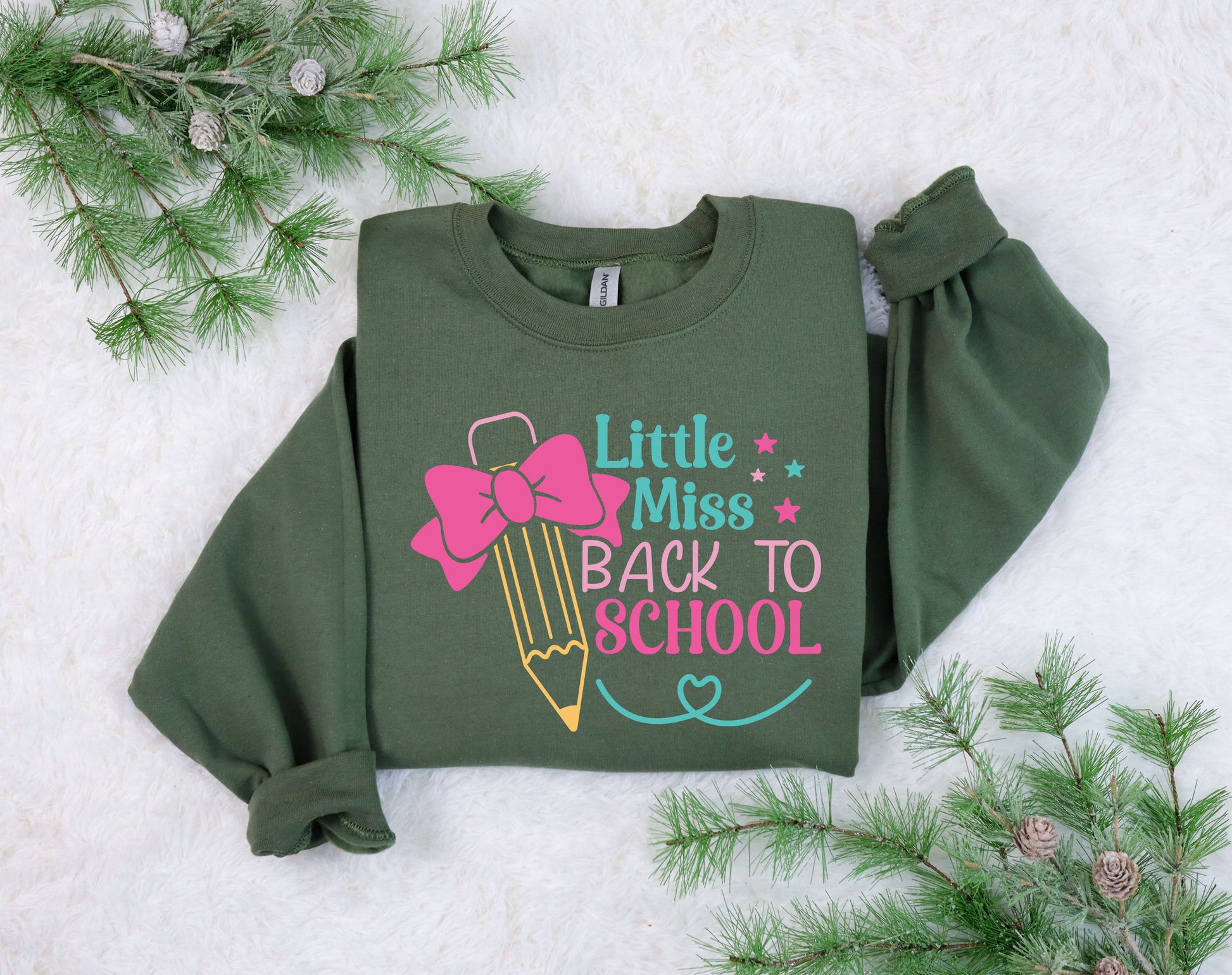 "Little Miss Back to School" DTF transfer design on a green sweatshirt featuring a yellow pencil with a pink bow, colorful stars, and playful text, perfect for back-to-school apparel.