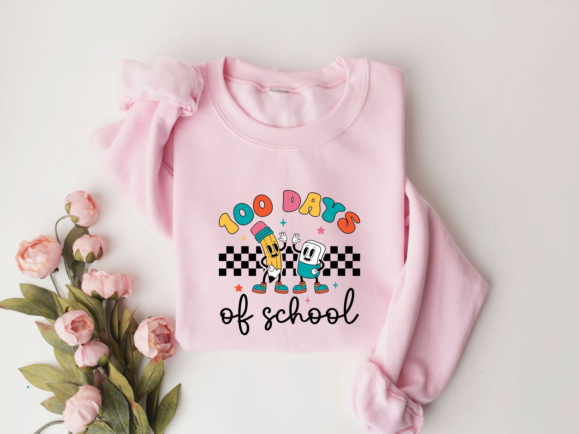 "100 Days of School" DTF transfer design on a pink sweatshirt featuring colorful letters, animated pencil and paper characters, checkered patterns, and playful stars, perfect for 100th-day-of-school celebrations.