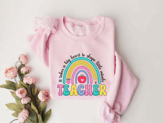 "It Takes a Big Heart to Shape Little Minds" Teacher DTF transfer design on a pink sweatshirt featuring a colorful rainbow, heart-shaped apple, and playful lettering, perfect for teacher appreciation apparel.