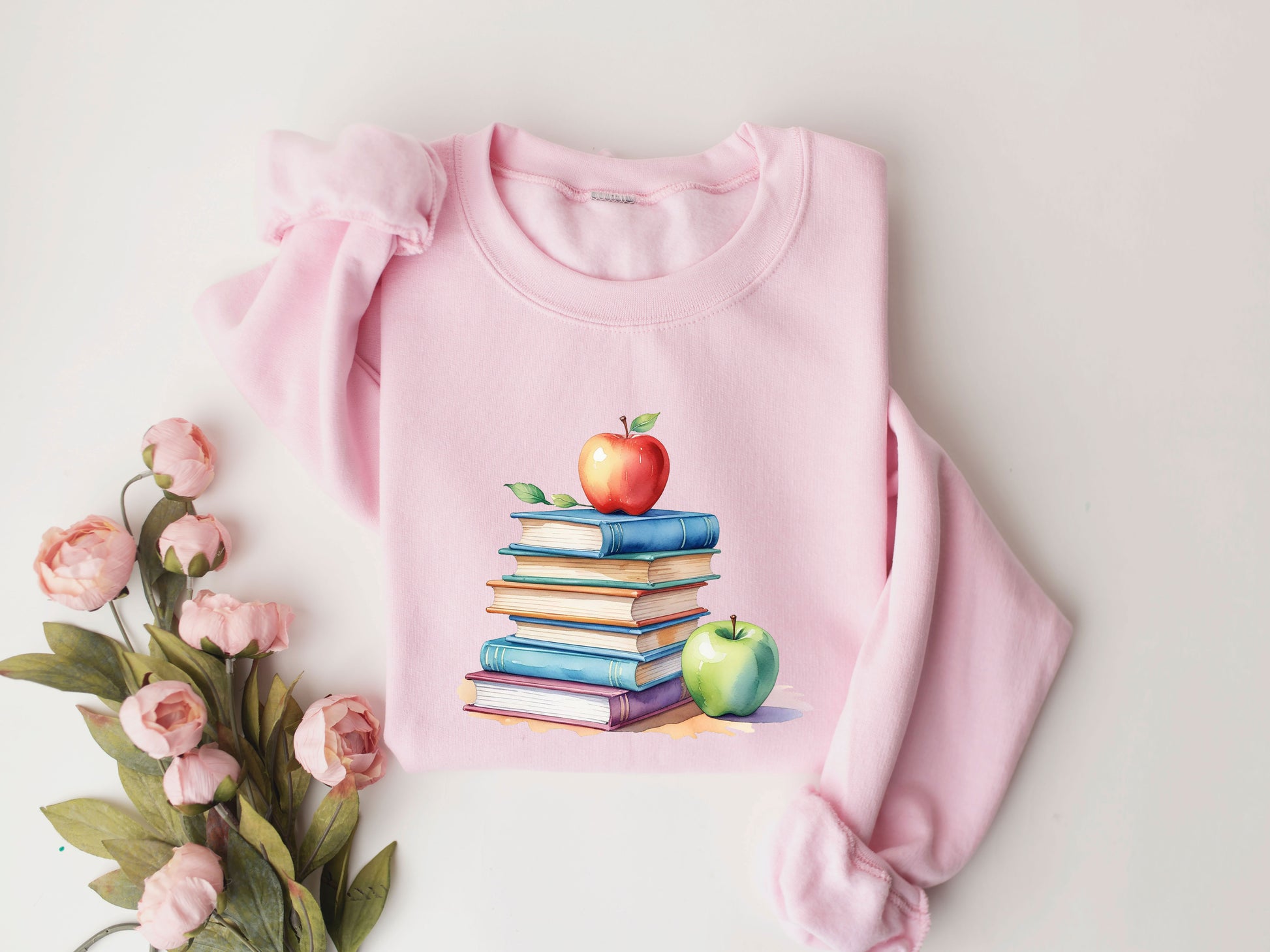 "Stack of Books with Apples" DTF transfer design on a pink sweatshirt featuring a colorful stack of books topped with a red apple and a green apple beside it, perfect for back-to-school apparel.