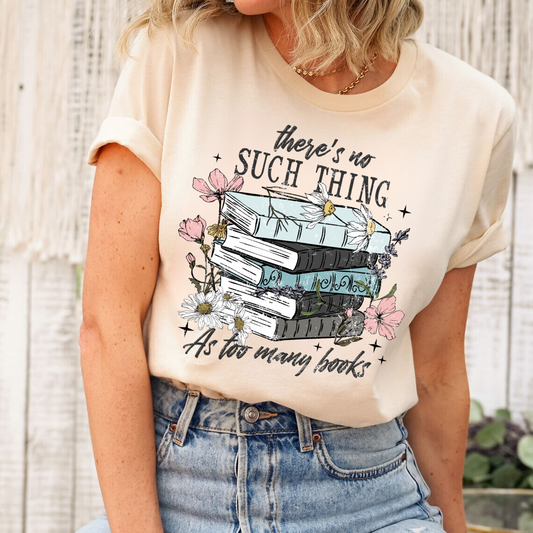 "There's No Such Thing as Too Many Books" DTF transfer design on a beige t-shirt featuring a stack of vintage books surrounded by pink and white flowers with elegant typography.