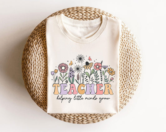 Beige sweatshirt featuring a "Teacher Helping Little Minds Grow" DTF transfer with colorful wildflowers and butterflies.