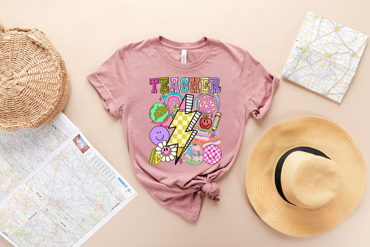 Pink t-shirt with a colorful retro teacher-themed DTF transfer featuring a lightning bolt, smiley faces, a globe, books, and pencils.