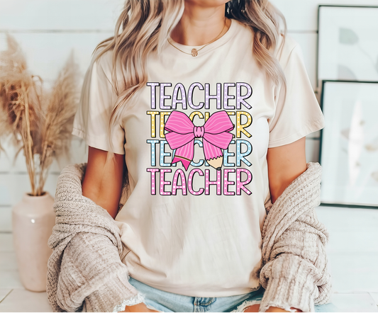 Beige t-shirt with pastel-colored "Teacher" text and pink pencil bow DTF transfer, perfect for teacher-themed apparel.