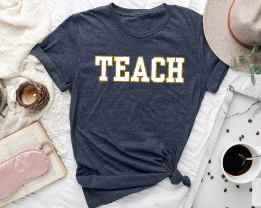 Dark blue t-shirt with bold collegiate-style TEACH lettering in yellow and white, perfect for educators.