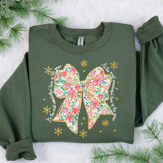 A festive green sweater featuring a colorful bow with floral patterns and golden snowflakes, complemented by seasonal wishes.