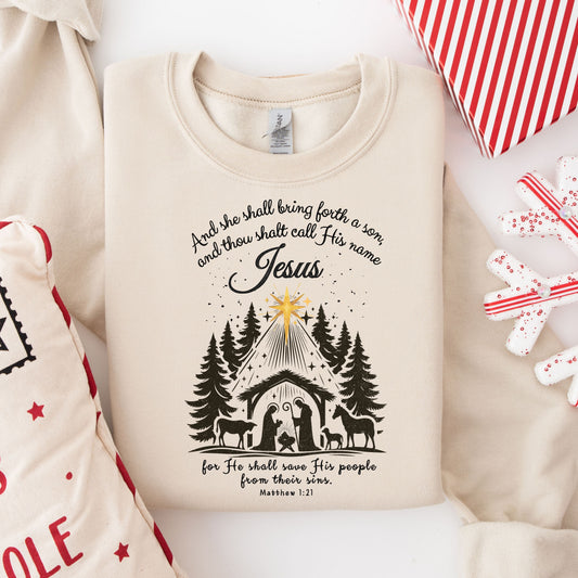 Christmas sweater featuring a nativity scene with the Holy Family under a star, accompanied by the verse Matthew 1:21.