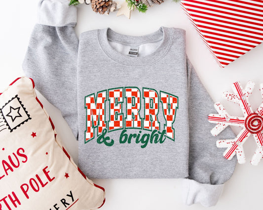 Merry & Bright" Christmas ready-to-press DTF transfer in green and red on a grey sweater, surrounded by holiday decorations