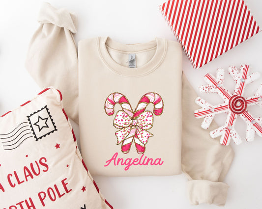 Customizable "Personalized Candy Cane Bow" DTF transfer on a beige sweatshirt, featuring a vibrant candy cane design with optional personalization.