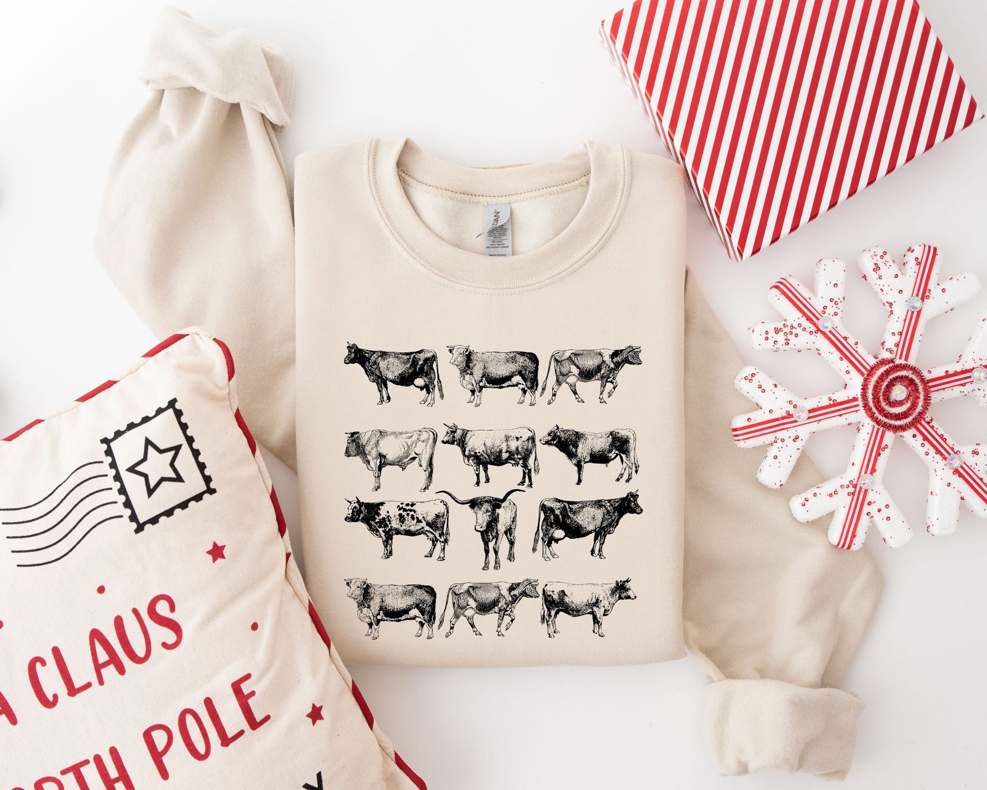 ountry Christmas cows DTF transfer design on a beige sweatshirt, featuring multiple cow illustrations in a charming row arrangement.