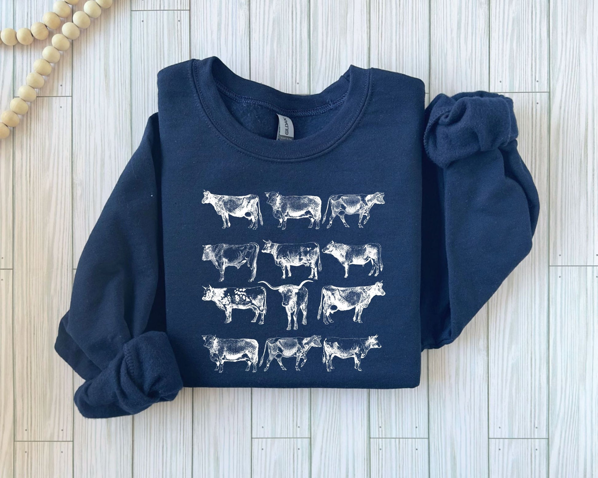 White cow prints on a navy blue sweatshirt, Christmas ready-to-press DTF transfer design featuring rows of unique cow silhouettes.