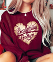 DTF Transfers ready to press – “Beautifully Broken” cracked heart design in vintage gold on a maroon sweatshirt, symbolizing healing and emotional strength.