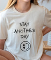 DTF Transfers ready to press – black handwritten “Stay Another Day” with semicolon symbol on neutral t-shirt, minimalist mental health awareness design.