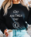 DTF Transfers ready to press – white handwritten “Stay Another Day” with semicolon symbol on black sweatshirt, clean mental health message design.