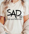 DTF Transfers ready to press – black handwritten-style “SAD Stay Another Day” mental health awareness design on neutral shirt, supporting suicide prevention.