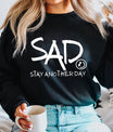 DTF Transfers ready to press – white handwritten “SAD Stay Another Day” mental health awareness design on black sweatshirt, powerful contrast and meaning.