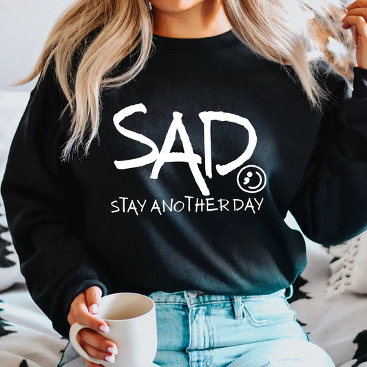 DTF Transfers ready to press – white handwritten “SAD Stay Another Day” mental health awareness design on black sweatshirt, powerful contrast and meaning.