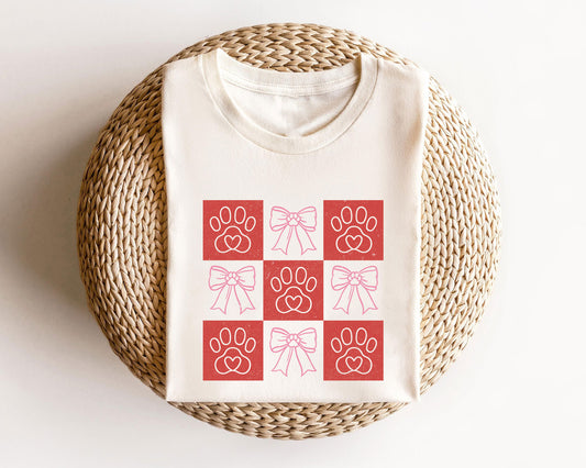 Grid of paw prints with hearts and pink bows ready-to-press DTF transfer design on a white T-shirt.