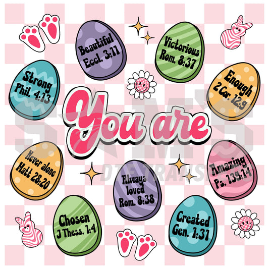 Assortment of colorful Easter eggs each inscribed with uplifting Bible verses, surrounded by 'You are' phrases, and playful springtime motifs.