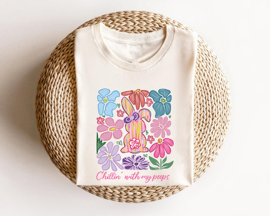 Cream-colored t-shirt featuring a pastel Easter Bunny design with colorful flowers and "Chillin' with My Peeps" text, perfect for Easter celebrations.