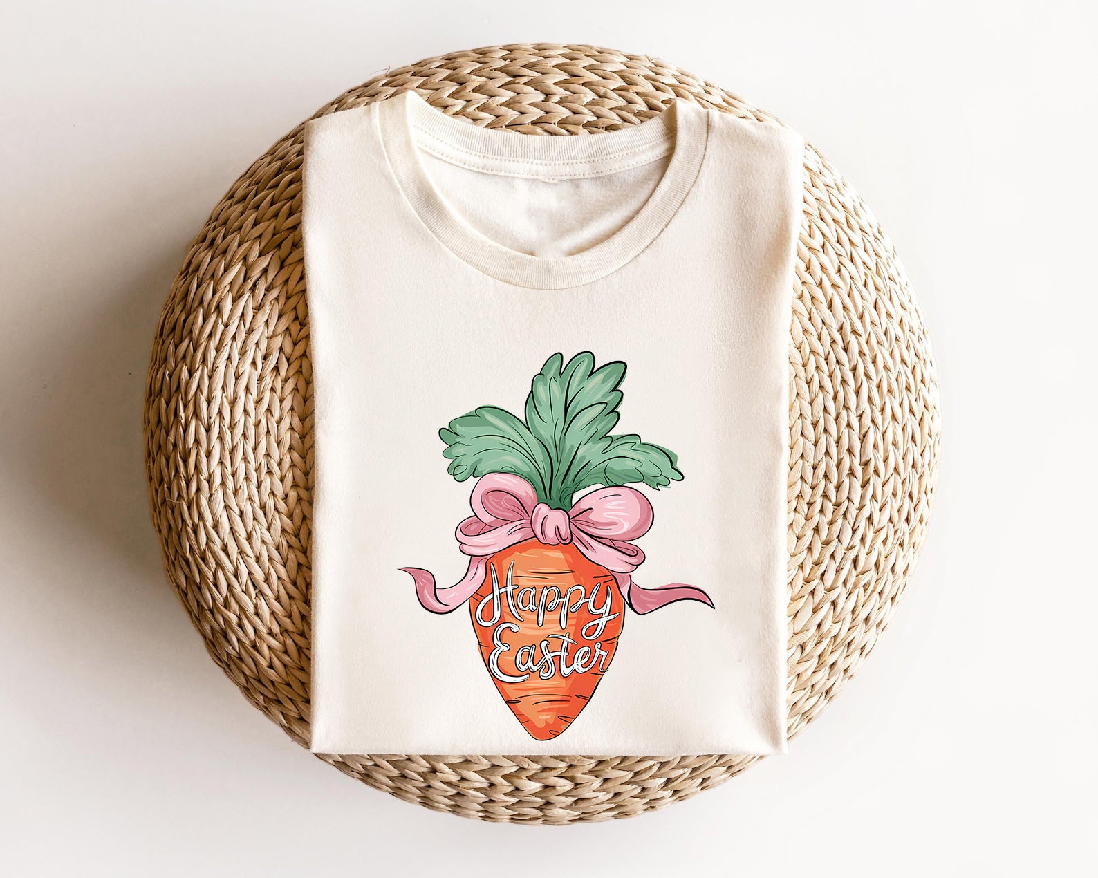 Cream-colored t-shirt featuring a hand-drawn carrot wrapped in a pink bow with "Happy Easter" text, perfect for festive Easter apparel.