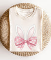 Cream t-shirt featuring white fluffy bunny ears and a pink bow with small bunny faces, perfect for Easter-themed designs.