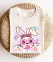 Cream t-shirt featuring a stylish bunny face with pink sunglasses, a cheetah bandana, and a pastel lilac checkerboard background—perfect for Easter apparel.