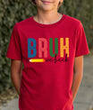 Red T-shirt with “BRUH We Back” DTF transfer design featuring large colorful block letters, a pencil graphic, and handwritten text.