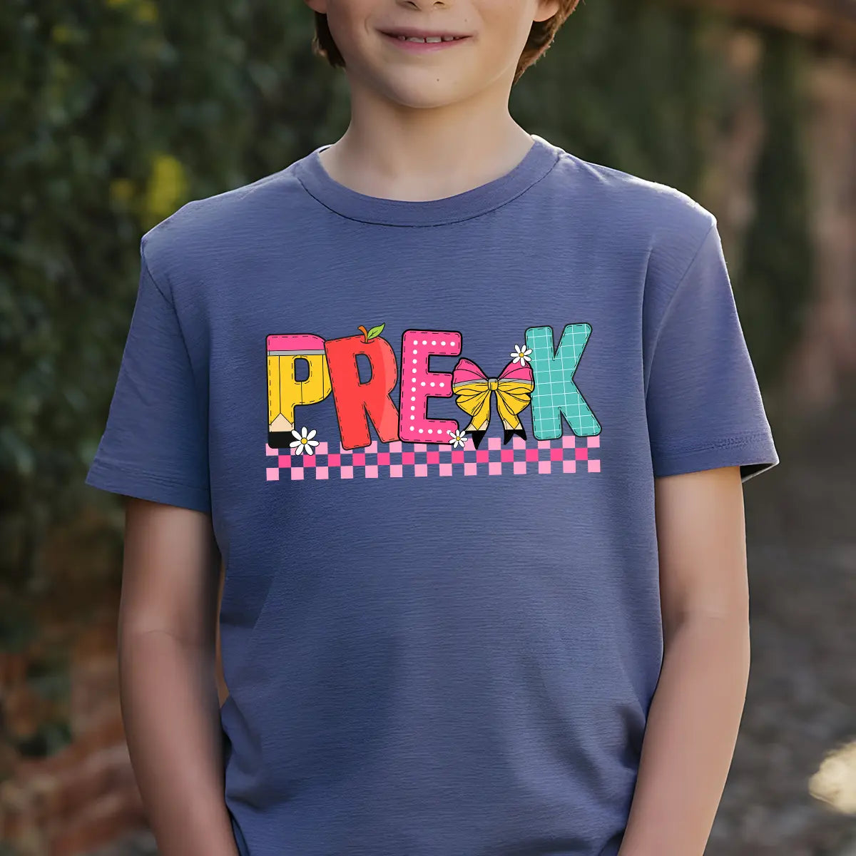 Navy T-shirt with colorful “PRE-K” DTF transfer design featuring school-themed letters, bow, daisies, and pink checkerboard accents.