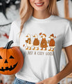 White T-shirt with “Just a Cozy Goose” DTF transfer design featuring four autumn-dressed geese with scarves, hats, and warm drinks.