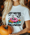 White T-shirt with “Just Waiting for Halloween” DTF transfer design featuring a skeleton in a pink pool float with pumpkins and bats.