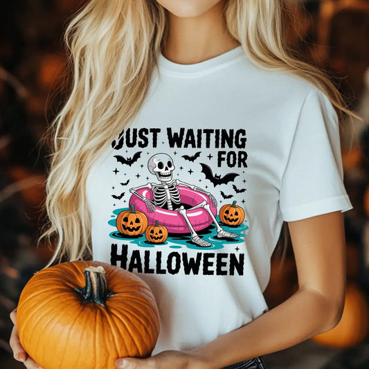 White T-shirt with “Just Waiting for Halloween” DTF transfer design featuring a skeleton in a pink pool float with pumpkins and bats.
