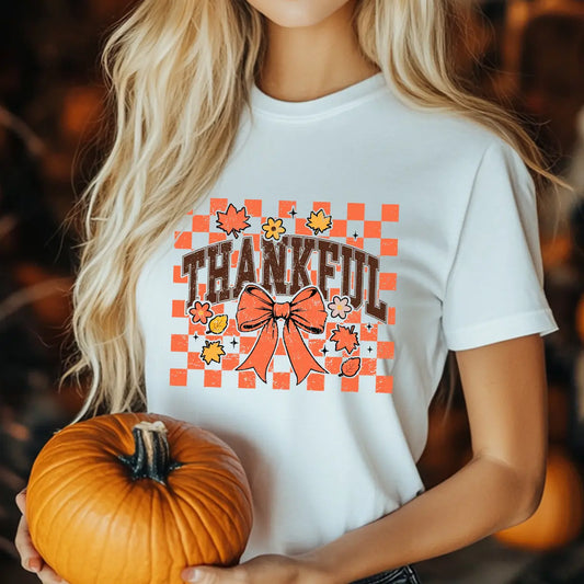 White t-shirt with “Thankful” checkered orange DTF transfer design featuring fall leaves and bow, perfect for Thanksgiving and autumn-themed apparel.