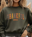 Green sweatshirt with bold rustic block letters reading “Thankful Teacher” in warm autumn colors with leaf accents, perfect for fall and Thanksgiving apparel.