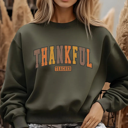 Green sweatshirt with bold rustic block letters reading “Thankful Teacher” in warm autumn colors with leaf accents, perfect for fall and Thanksgiving apparel.