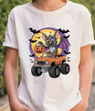 White t-shirt with colorful Halloween design featuring a cartoon bat in an orange monster truck, jack-o’-lantern candy bucket, bats, and full moon background.