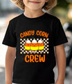 Black t-shirt with design featuring three smiling candy corns wearing sneakers, checkerboard background, and bold orange text “Candy Corn Crew.”