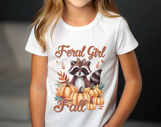 White t-shirt with autumn design featuring a raccoon with leopard bow surrounded by pumpkins and fall leaves, text “Feral Girl Fall” in script style.