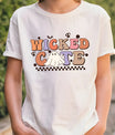 White t-shirt with Halloween design featuring retro bubble letters “Wicked Cute,” peace-sign ghost, checkerboard base, bats, and skulls.